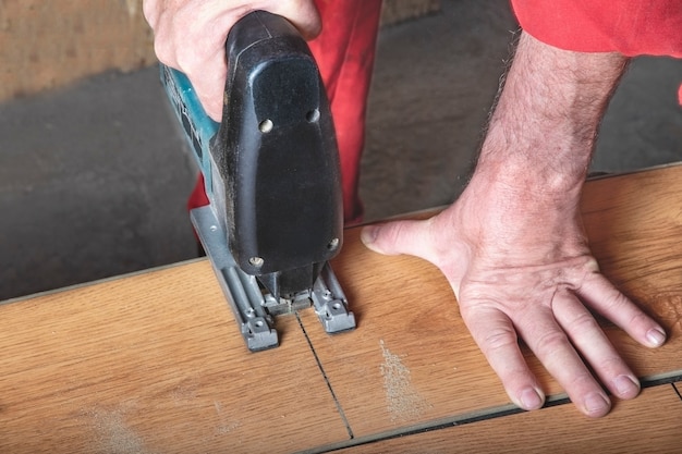 un ouvrier en combinaison rouge coupe un stratifié avec une scie sauteuse en marquant le sien au repos dans l'atelier