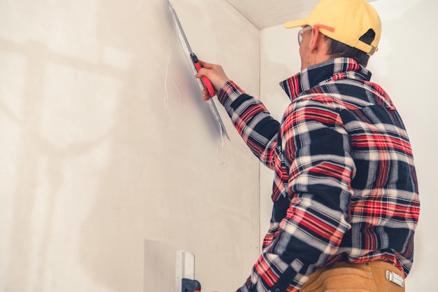 Un ouvrier de la construction appose du plâtre sur des murs intérieurs