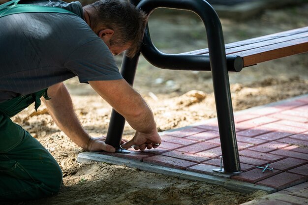 Un ouvrier de la construction attache un banc de parc à des pierres de pavage