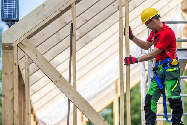 Ouvrier de construction à ossature de squelette de maison en bois dans la quarantaine sur la charpente de toit nouvellement construite