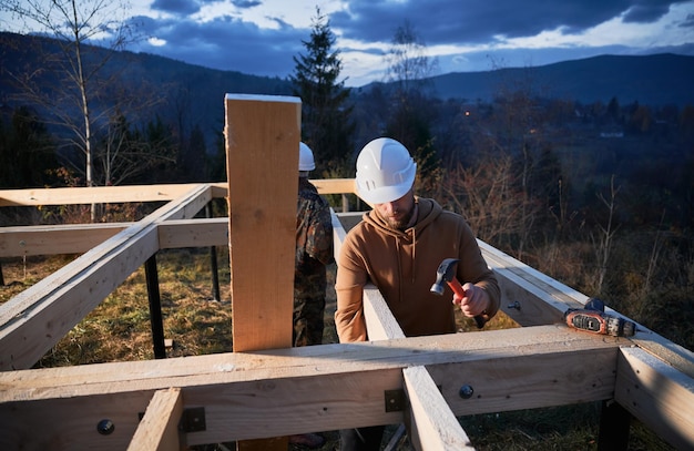 Un ouvrier construit une maison en charpente de bois sur une fondation de pile