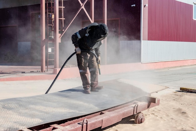 Un ouvrier en costume spécial sablage du métal sur un site industriel.