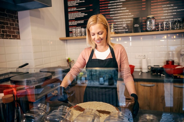 Un ouvrier de crêperie met du chocolat sur des crêpes tout en souriant