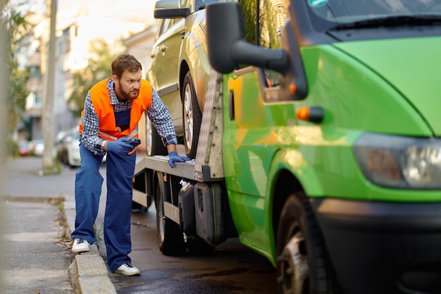 Ouvrier de dépanneuse concentré en uniforme vérifiant la précision du chargement de la voiture. Préparation à l'évacuation