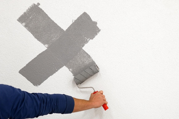 Ouvrier a dessiné une croix avec un rouleau sur le mur blanc