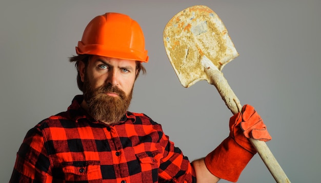 Ouvrier du bâtiment barbu en casque avec constructeur de bêche en gants de travail avec pelle