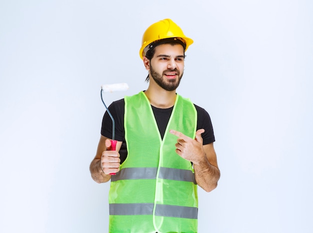 Ouvrier du bâtiment avec un casque jaune tenant un rouleau de finition blanc.