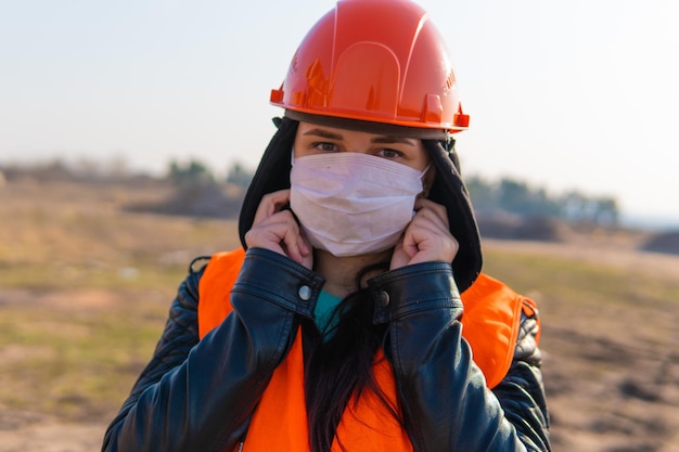 Ouvrier du bâtiment féminin en salopette mettant un masque médical sur le visage sur la zone de construction