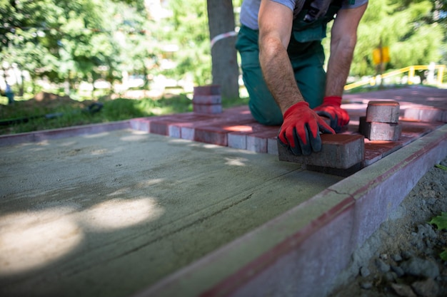 Un ouvrier du bâtiment habile pose des pavés rouges sur un trottoir