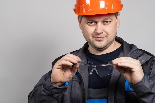 Un ouvrier du bâtiment portant un casque et une combinaison met des lunettes de protection sur un fond blanc