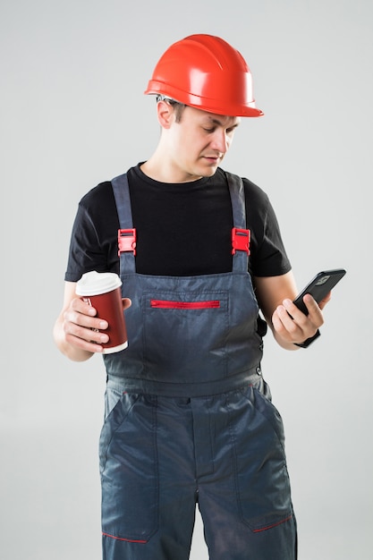 Ouvrier du bâtiment souriant dans le casque de boire du café pour aller utiliser le téléphone