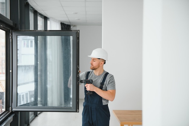 Ouvrier du bâtiment utilisant une perceuse lors de l'installation d'une fenêtre à l'intérieur