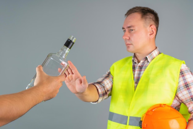 Un ouvrier du bâtiment en vêtements de travail refuse une bouteille d'alcool fort offerte. Refus de boire au travail
