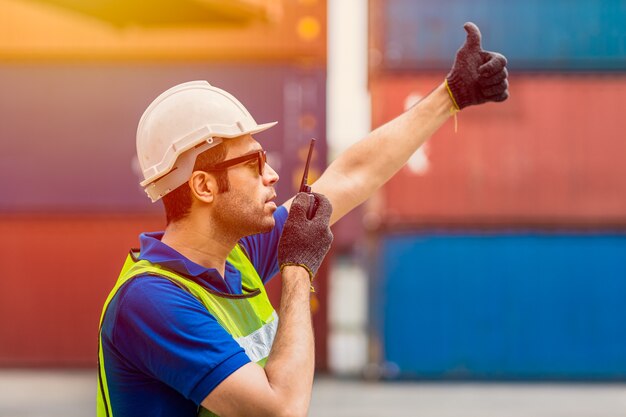 Ouvrier du personnel d'expédition du contremaître travaillant à la radiocommande chargeant la logistique du port de fret pour les marchandises d'importation et d'exportation dans l'entrepôt de conteneurs.