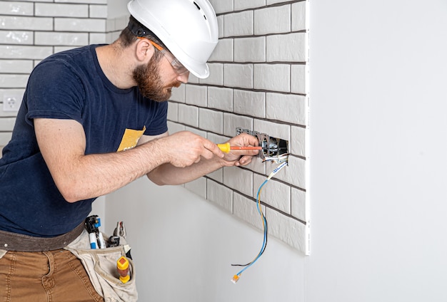 Ouvrier électricien avec une barbe en salopette lors de l'installation de prises. Concept de rénovation domiciliaire.