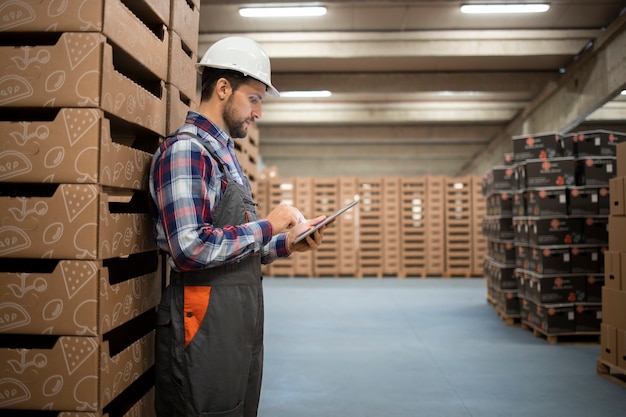 Ouvrier d'entrepôt du Caucase vérifier l'inventaire des marchandises sur ordinateur tablette dans la salle de stockage de l'usine.