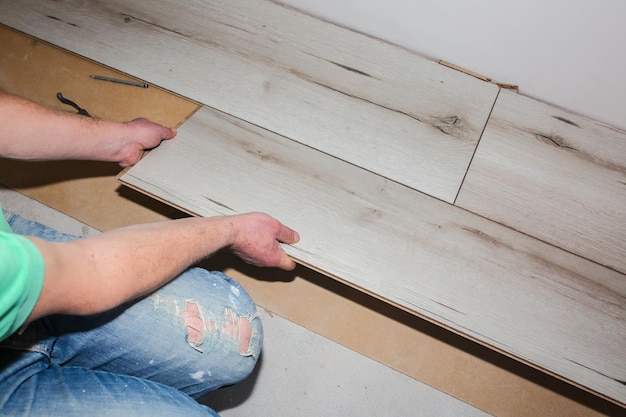 Ouvrier fabriquant des sols stratifiés dans un appartement Rénovation de réparation d'entretien Planches de parquet en bois à l'intérieur