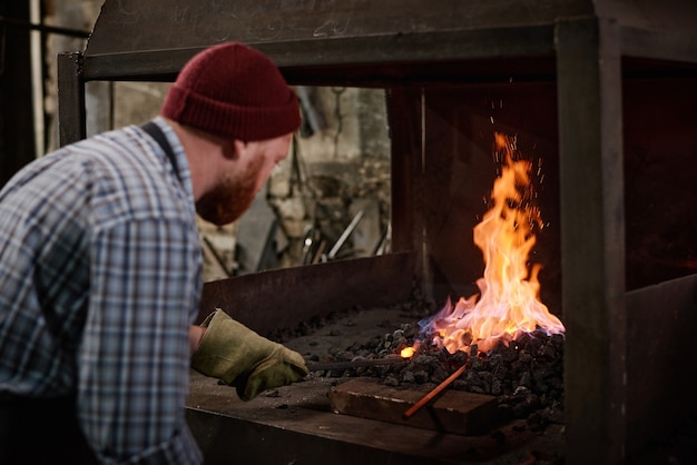 Ouvrier en gants de protection ajoutant des charbons pour brûler la flamme dans le four