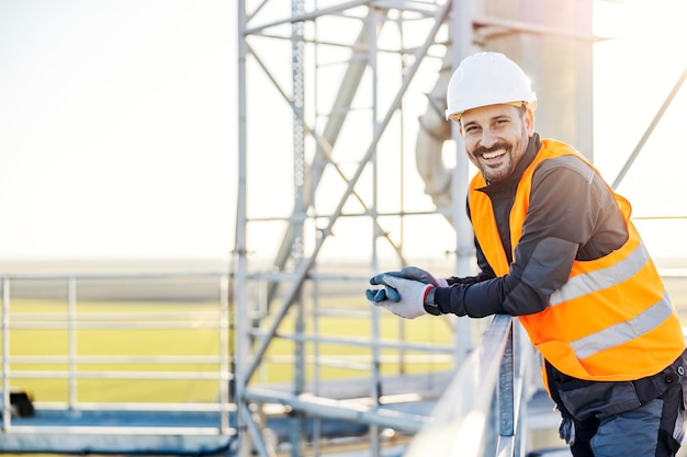 Un ouvrier de l'industrie s'appuyant sur la balustrade en hauteur et souriant à la caméra