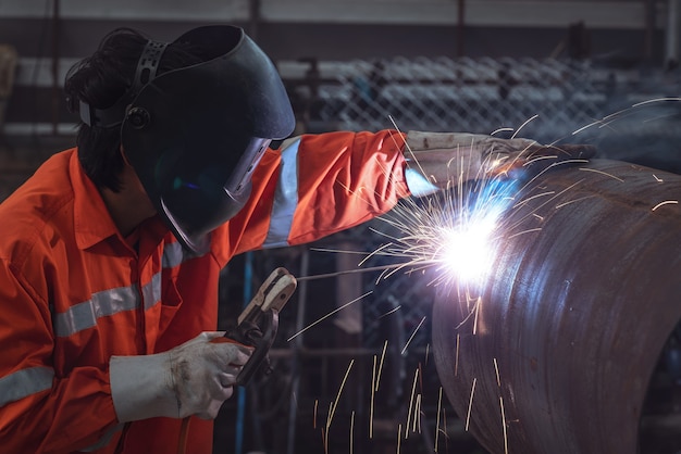 Ouvrier industriel avec masque de protection soudant une structure en acier dans une usine