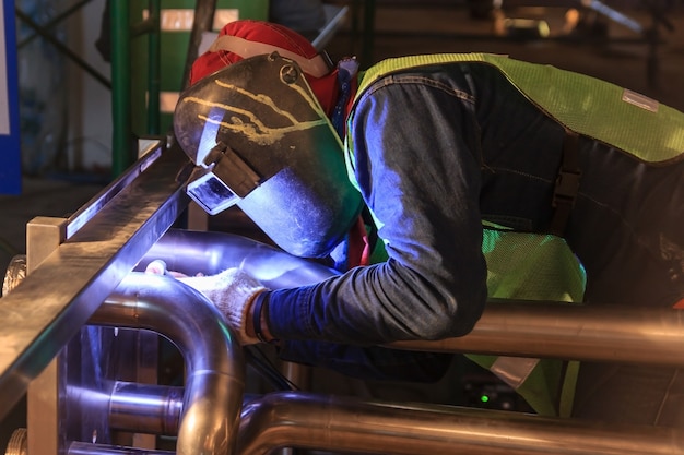 Ouvrier industriel avec masque de protection soudant une tuyauterie en métal à l&#39;aide d&#39;une soudeuse tig