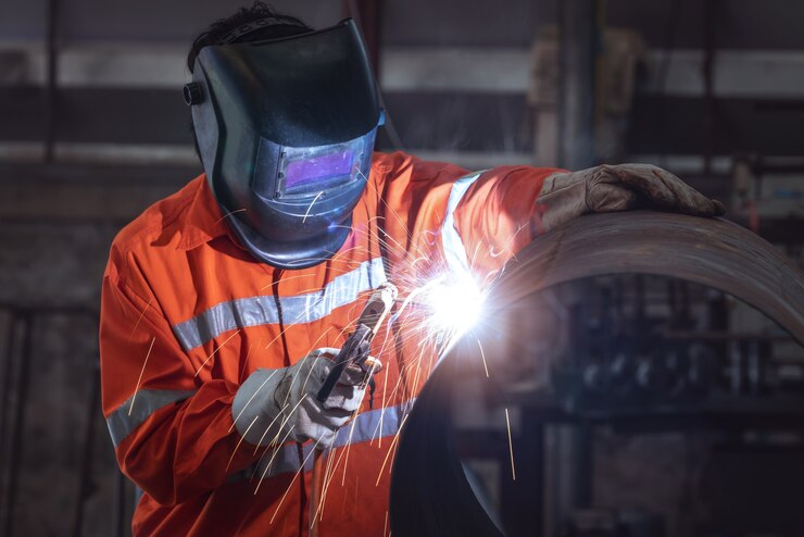 Ouvrier industriel avec masque de protection soudant des tuyaux métalliques dans une usine