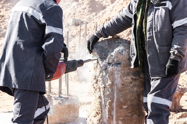 Un ouvrier avec un marteau-piqueur casse des pieux en béton Abattage de la tête de pieu avec un outil à main Préparation des pieux pour le montage de la fondation