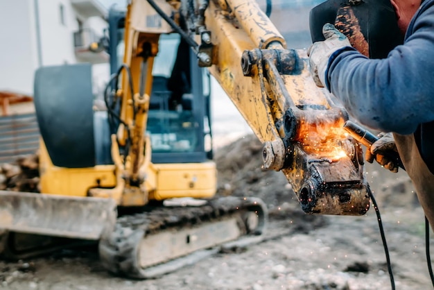 Photo ouvrier professionnel soudant le bras de l'excavatrice sur le chantier de construction