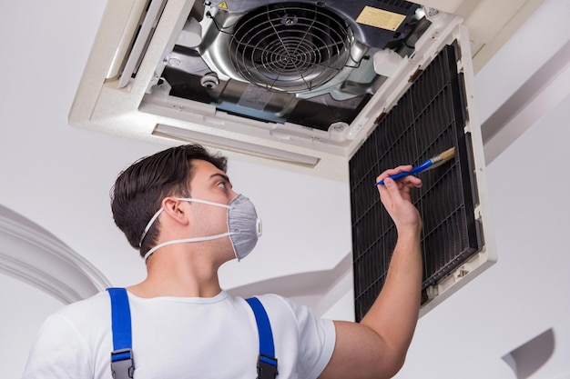 Photo ouvrier réparant une unité de climatisation au plafond