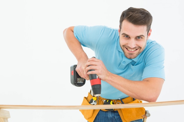 Ouvrier souriant à l&#39;aide de la perceuse à main sur une planche en bois