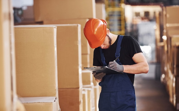 Un ouvrier de stockage en uniforme et un bloc-notes en mains vérifie la production.