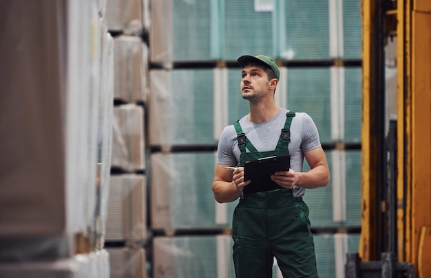 Un ouvrier de stockage en uniforme de couleur verte et un bloc-notes à la main vérifie la production.