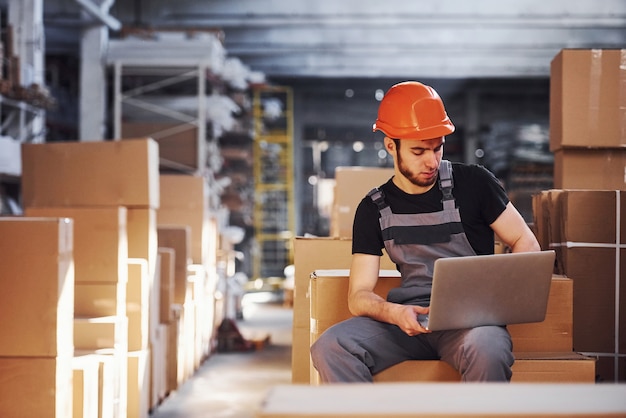 Un ouvrier de stockage en uniforme et un ordinateur portable moderne en mains vérifie la production.