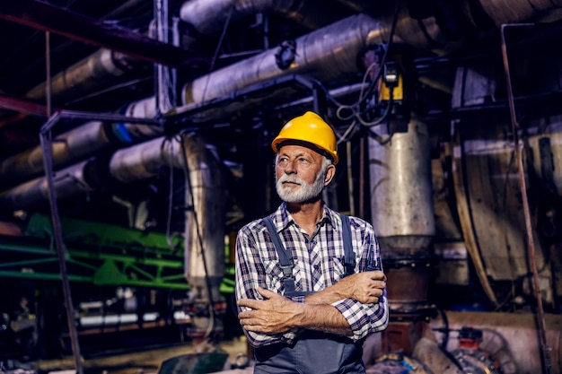 Un ouvrier supérieur réussi avec un casque sur sa tête se tient dans l'usine