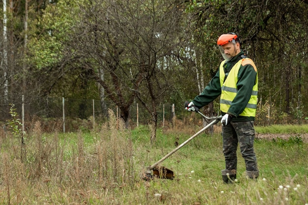 Un ouvrier en tenue professionnelle tond l'herbe avec une tondeuse