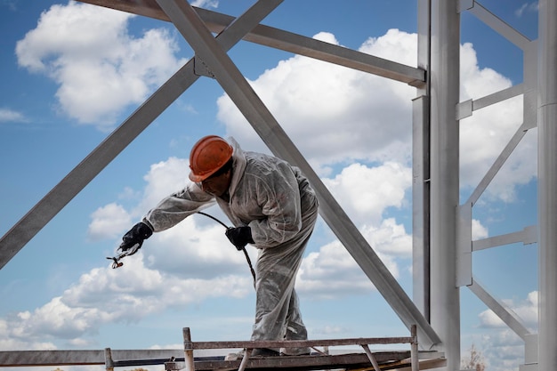 Un Ouvrier En Tenue De Protection Spéciale, Travaille à La Peinture Et à La Protection Incendie Des Structures Métalliques En Hauteur. Peinture Du Métal Sur Le Chantier.