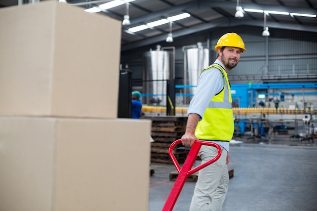 Ouvrier tirant un chariot de boîtes en carton en usine