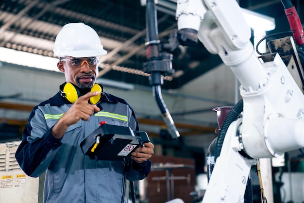 Photo ouvrier d'usine afro-américain travaillant avec un bras robotique adepte