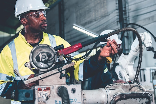 Ouvrier d'usine afro-américain travaillant avec un bras robotique adepte