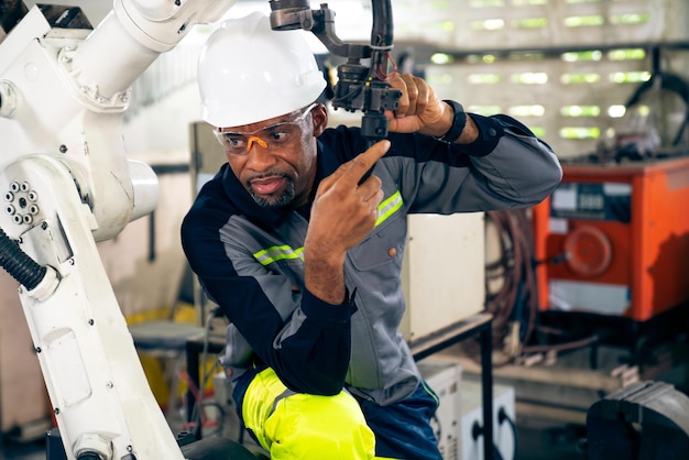 Ouvrier d'usine afro-américain travaillant avec un bras robotique adepte