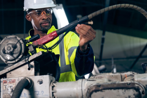 Ouvrier d'usine afro-américain travaillant avec un bras robotique adepte