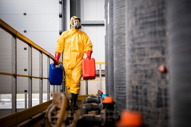 Ouvrier d'usine en combinaison de matières dangereuses et masque à gaz transportant des bidons en plastique contenant des produits chimiques