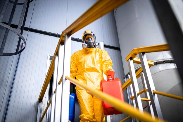 Ouvrier d'usine portant une combinaison de protection et un masque à gaz transportant des produits chimiques dans une usine industrielle