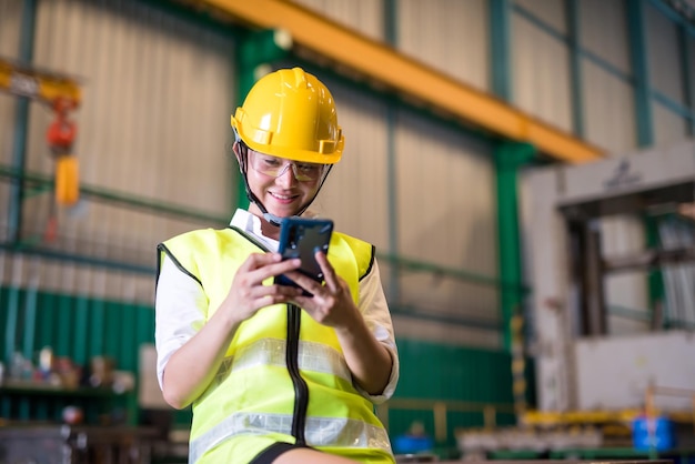 Une ouvrière asiatique d'usine à la taille haute utilise son smartphone pour jouer aux réseaux sociaux.