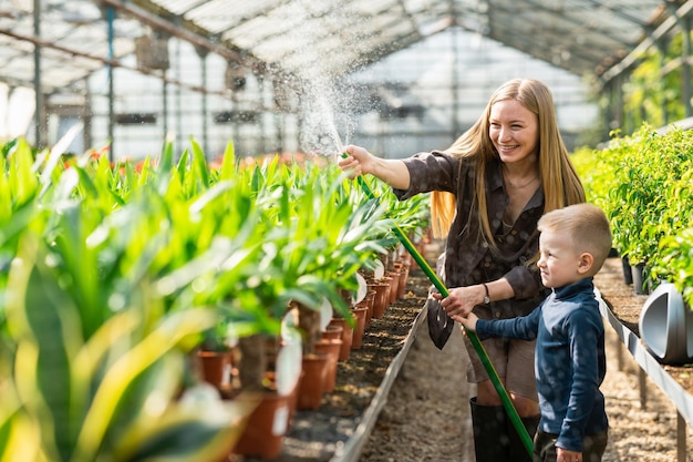 Ouvrière de serre avec son fils arrosant les plantes avec un tuyau