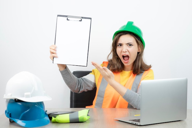 Ouvrière en uniforme assise au bureau avec ordinateur portable et presse-papiers. Photo de haute qualité