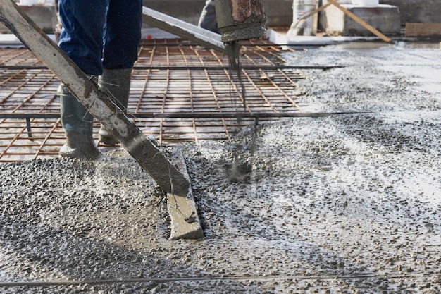 Ouvriers constructeurs coulent le sol en béton dans un atelier industriel Jambes dans des bottes en béton Soumission de béton pour couler le sol Travaux de béton monolithique