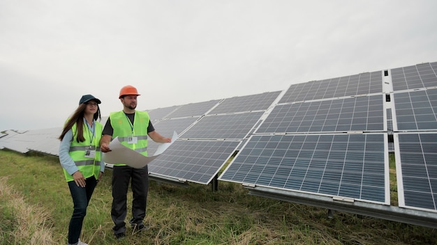 Ouvriers d'ingénieurs tenant un plan solaire dans les mains et debout près de la station de panneaux solaires