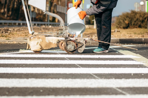 Les ouvriers routiers utilisent des machines à tracer pour peindre le passage pour piétons sur l'asphalte dans la ville