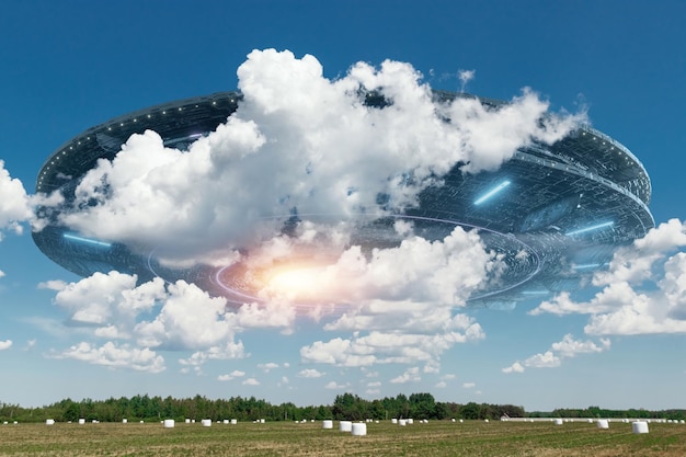 OVNI une soucoupe extraterrestre planant au-dessus du champ dans les nuages planant immobile dans le ciel Objet volant non identifié invasion extraterrestre vie extraterrestre voyage dans l'espace vaisseau spatial techniques mixtes